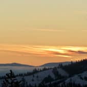 سماء غروب الشمس البرتقالية فوق الجبال مغطاة بالأشجار والثلوج.