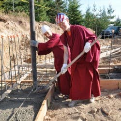 Venerable Chodron and Venerable Tarpa wear hard hats and pour concrete on the Chenrezig Hall construction site.
