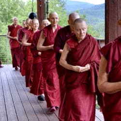 Sravasti Abbey monastics chant while walking in a single file on an outdoor deck.