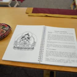 Prayer beads next to a prayer book open to a picture of Vajrasattva and the sadhana.