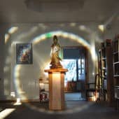Wooden Kuan Yin statue on a pedestal with an aura of light around it.