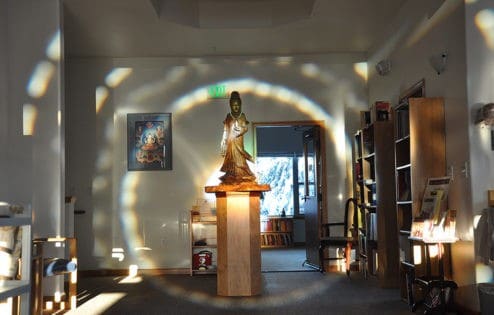 تمثال خشبي كوان يين على قاعدة مع وجود هالة من الضوء حوله.