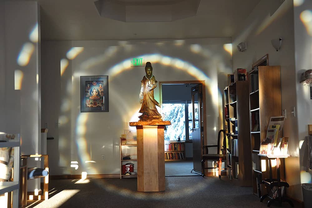 Wooden Kuan Yin statue on a pedestal with an aura of light around it.