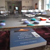 A copy of the book "Don't Believe Everything You Think" on the teacher's table facing a room with meditation cushions.
