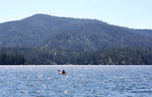 A solo person kayaks in a lake with mountains in the background.