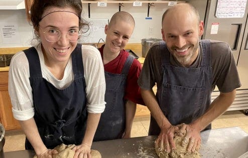 Young people knead bread together in the Sravasti Abbey kitchen.