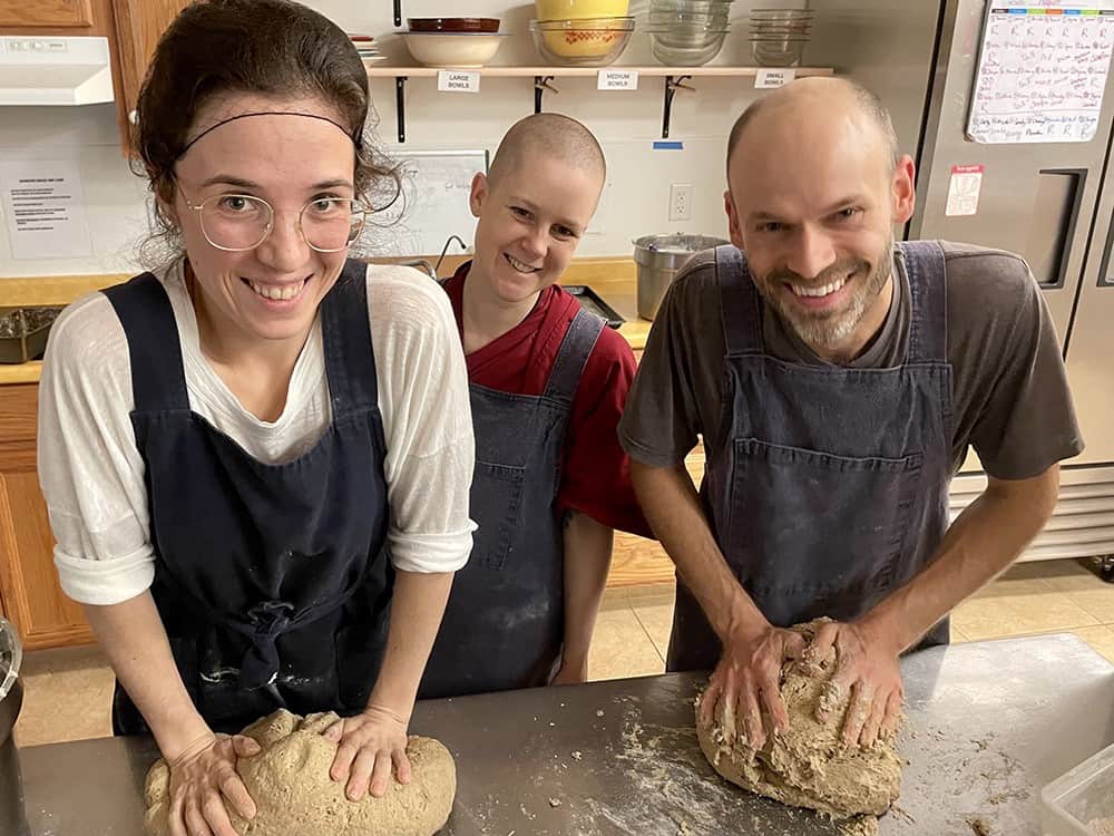 Young people knead bread together in the Sravasti Abbey kitchen.