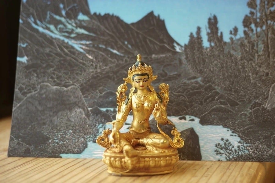Golden Tara statue in front of a card showing a river and mountains.