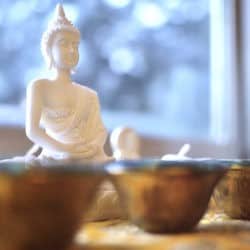Buddha statue and water bowls on altar in front of a window.