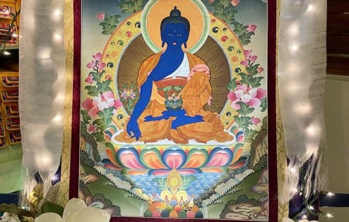 Medicine Buddha thangka surrounded by light and flower offerings.
