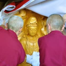 Venerables Chodron, Tarpa, and Semkye unveil a wooden Kuan Yin statue in a crate.