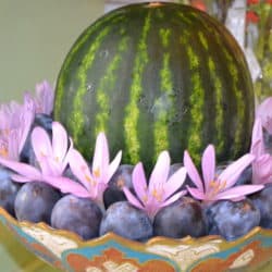 Fruit offering bowl containing watermelons, plums, and pink flowers.