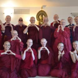Sravasti Abbey monastics make heart shapes with their hands in front of a Kuan Yin statue.