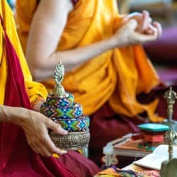 Tibetan monastics making the mandala offering mudra and using a mandala offering set to make offerings.