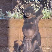 A statue of Maitreya Buddha with hands raised and laughing in the sun.
