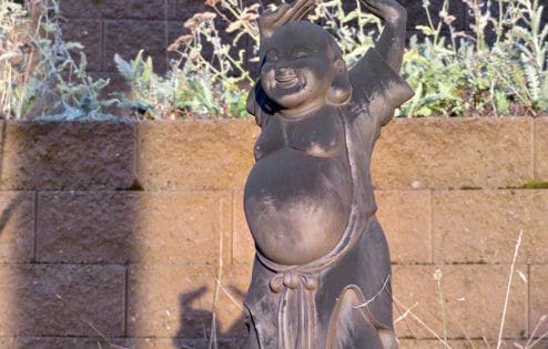 Socha Maitreya Buddha se zdviženýma rukama a smějící se na slunci.