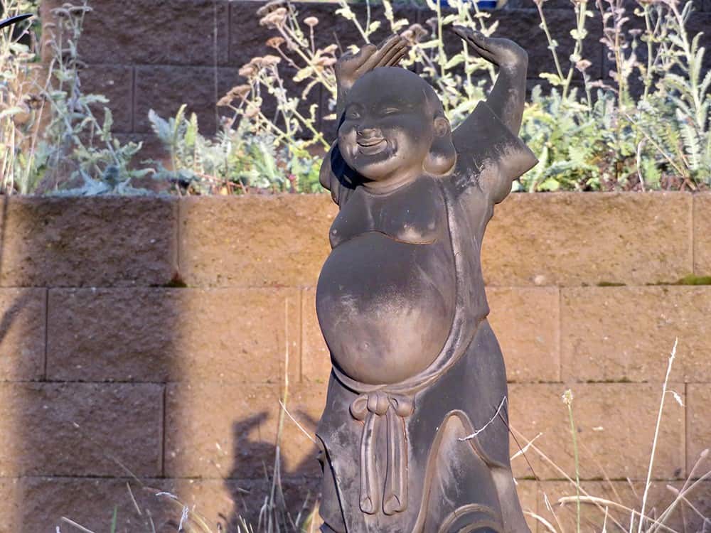 A statue of Maitreya Buddha with hands raised and laughing in the sun.