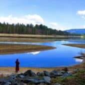 A nun stands at the edge of a lake reflecting a brilliant clear blue sky.
