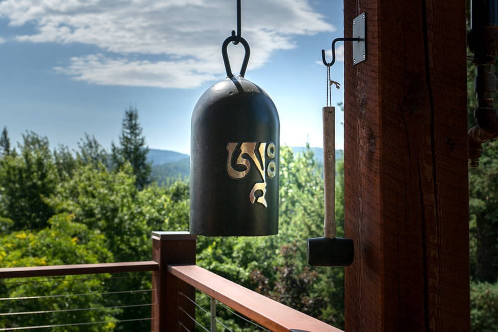 Bell with om symbol and its striker hanging on a deck overlooking landscape.