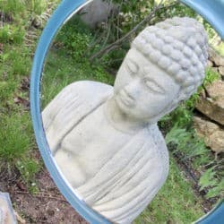 The reflection of a Buddha statue in the garden in a hand mirror.