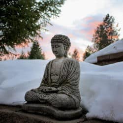 Statue of Buddha seated in meditation against a bank of snow.