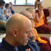 A row of monastics and trainees chanting with eyes closed and palms together.