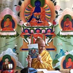 Venerable Chodron holds a copy of "Practical Ethics and Profound Emptiness" in front of a Medicine Buddha thangkha.