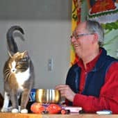 Dr Roger Jackson uśmiecha się do kota Maitri spacerującego po stole nauczycielskim.