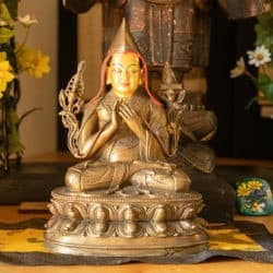 Statue of Lama Tsongkhapa on an altar with flowers in the background.