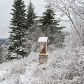Buddha statue in a glass house in a meadow covered in snow.