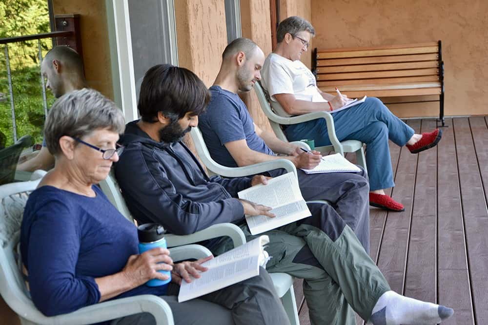 Four guests sit and read in chairs on the deck of Chenrezig Hall.