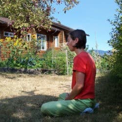 A young woman sits in meditation in the garden under a tree.