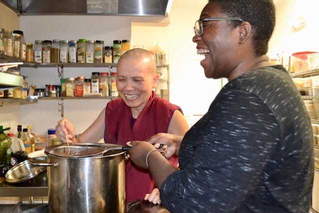 Rashika laughing while cooking in the Sravasti Abbey kitchen with Venerable Penne.