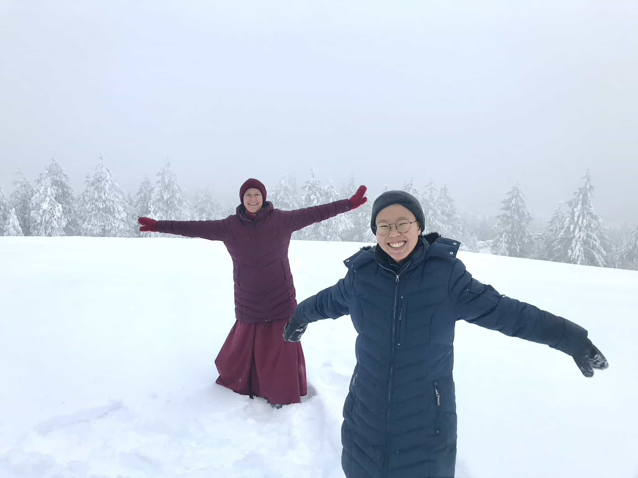 Dronsel and a monastic smiling with arms out, in a snowy meadow.
