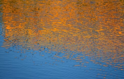غروب الشمس البرتقالي ينعكس في المياه المتموجة.