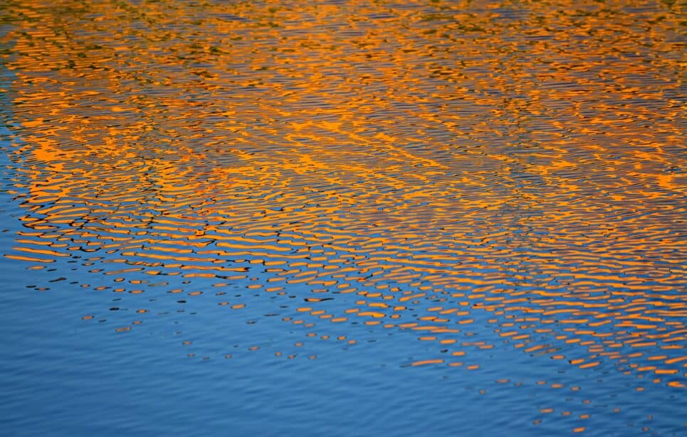 Orange sunset reflected in rippling water.