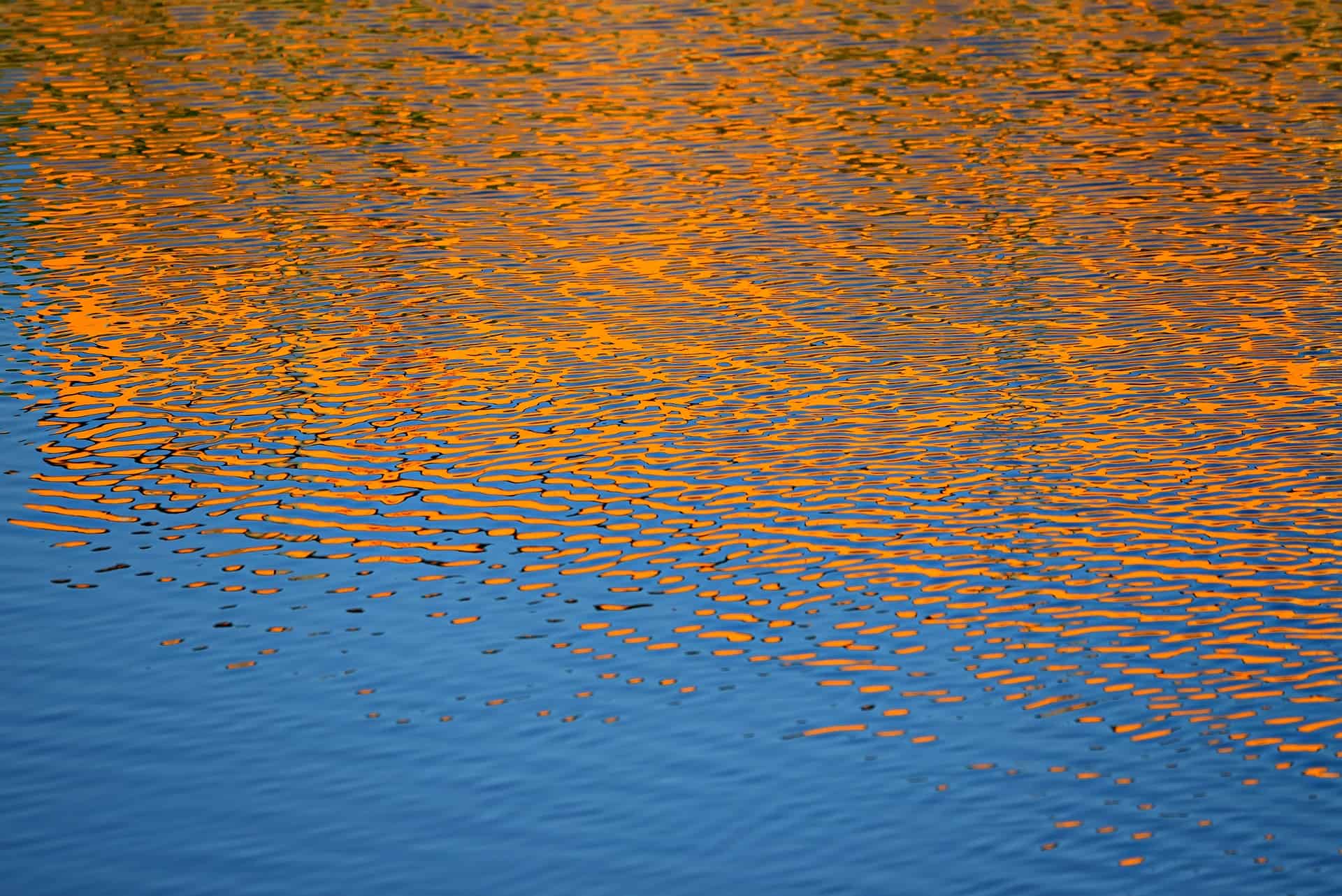 Orange sunset reflected in rippling water.