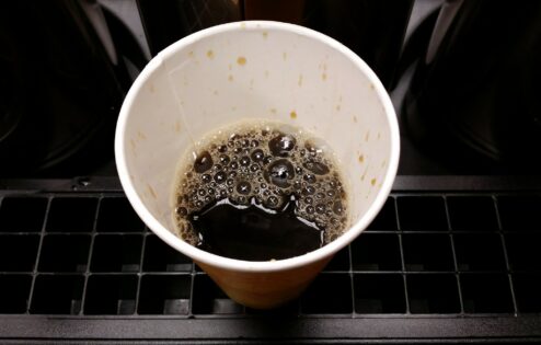Половина полной чашки кофе в бумажном стаканчике.