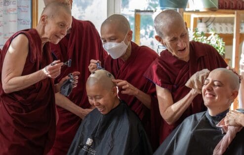 Two senior monastics help shave the heads of anagarikas before their ordination ceremony.