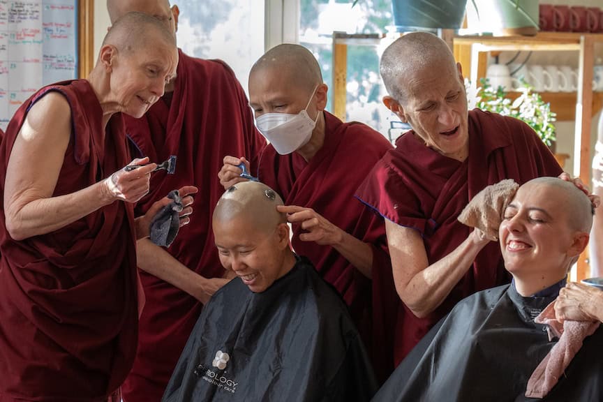 Two senior monastics help shave the heads of anagarikas before their ordination ceremony.